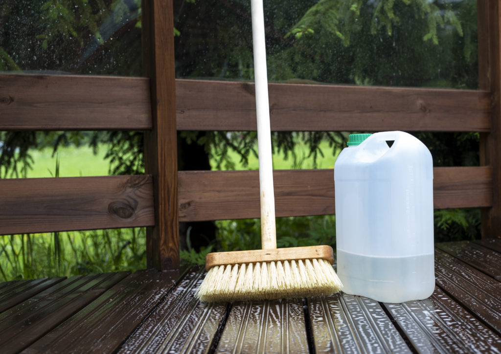 Brush, plastic canister with chemical solution and soap solution on the wooden planks of the terrace.